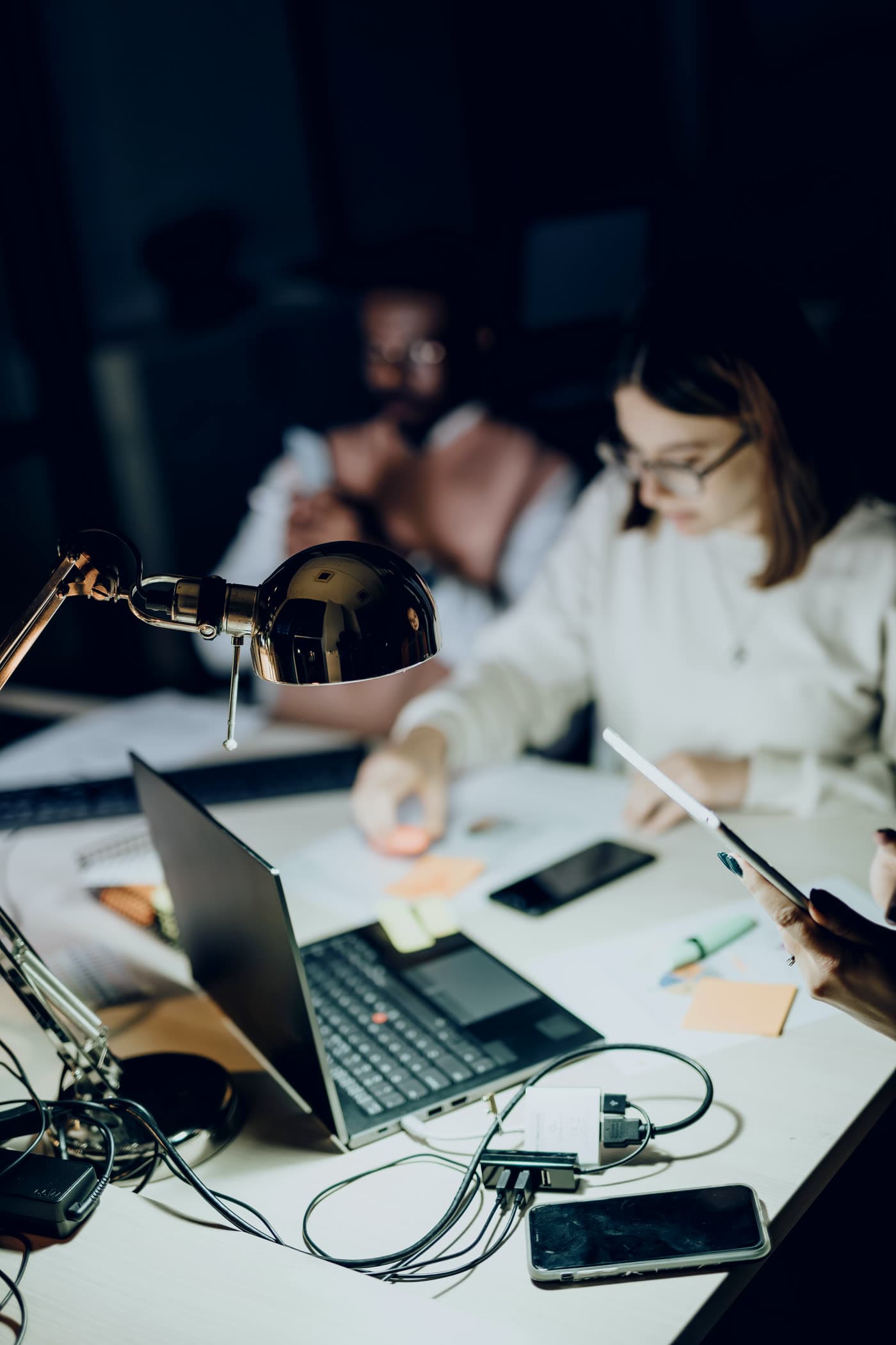 Equipe trabalhando à noite com notebook e relatórios sob a luz de uma luminária