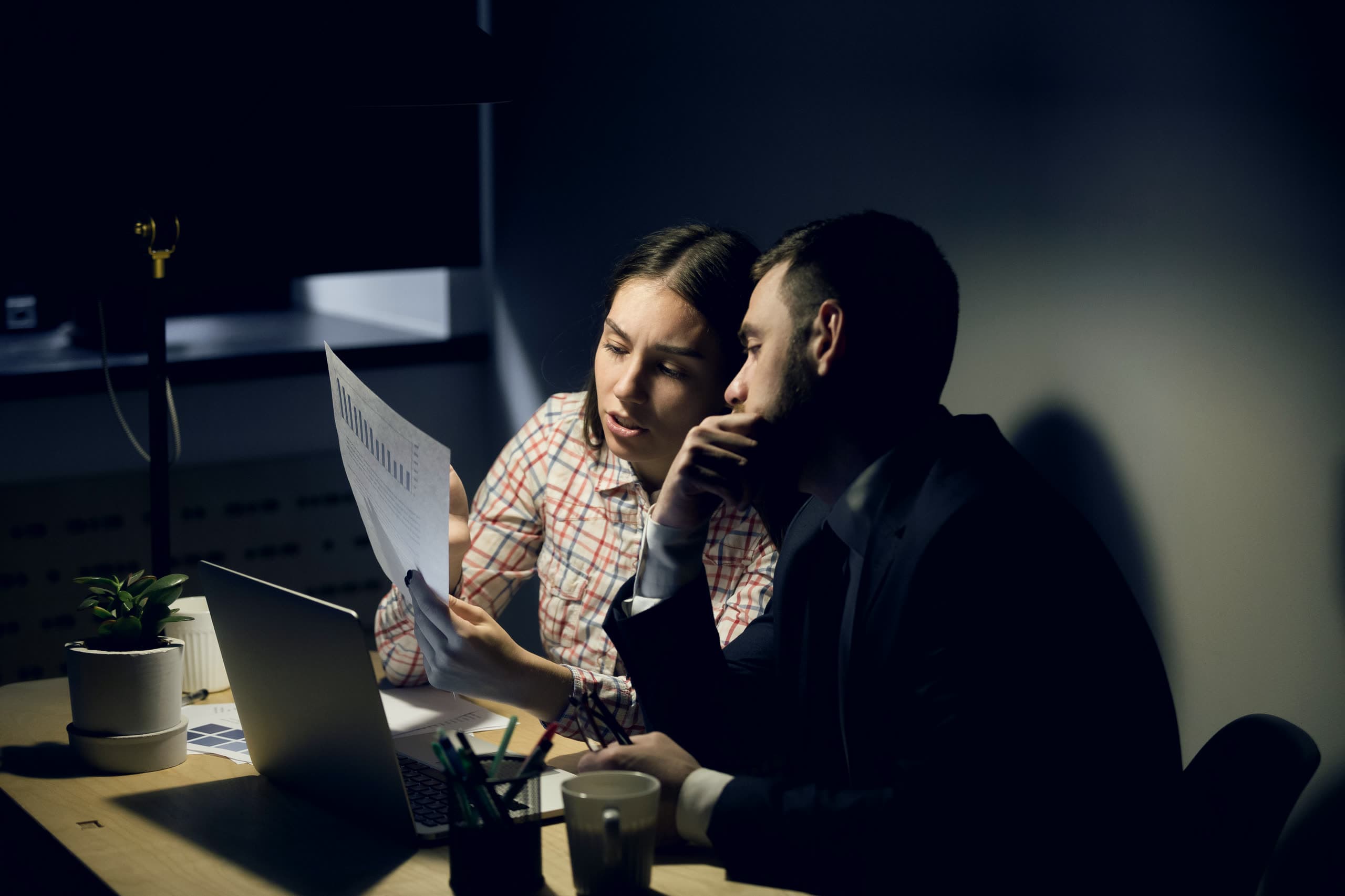 Duas pessoas analisando relatórios impressos em um escritório à noite